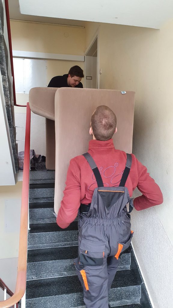 Mitarbeiter von Martens Transport tragen ein Sofa eine Treppe hinunter